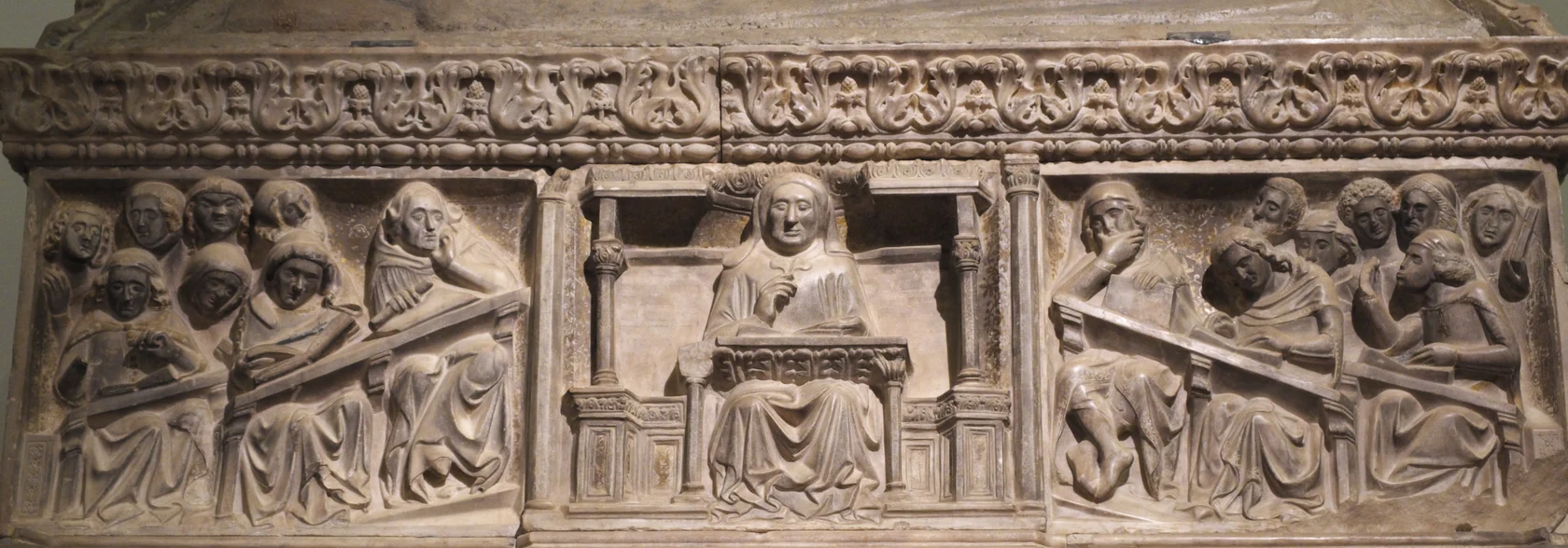 Marble relief of a professor lecturing from a reading desk, with students at slanted desks and open books on both sides